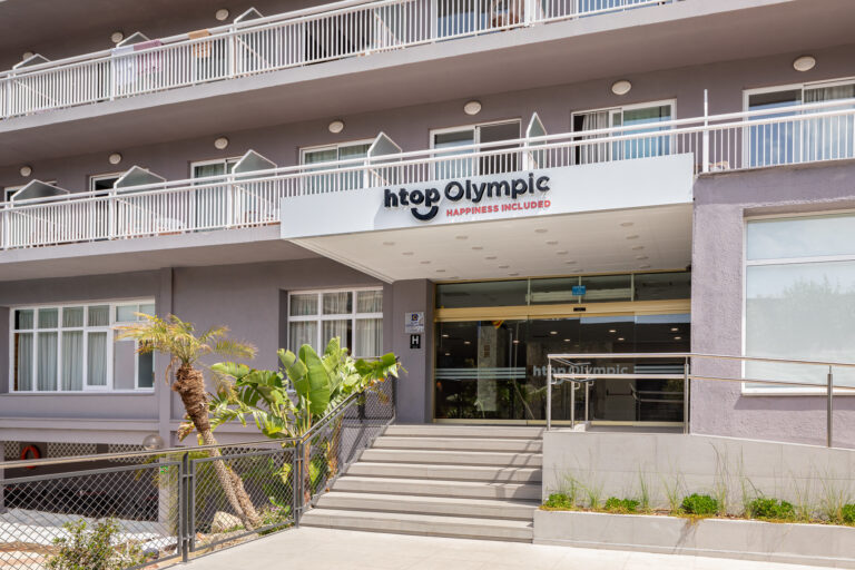 Der einladende Eingang des htops Olympic Hotels, mit einer modernen Fassade und einem klaren Schild, das den Namen des Hotels hervorhebt. Der Bereich ist von grünen Pflanzen umgeben, die für eine angenehme Atmosphäre sorgen.